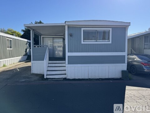 A grey and white mobile home with a car parked in front.