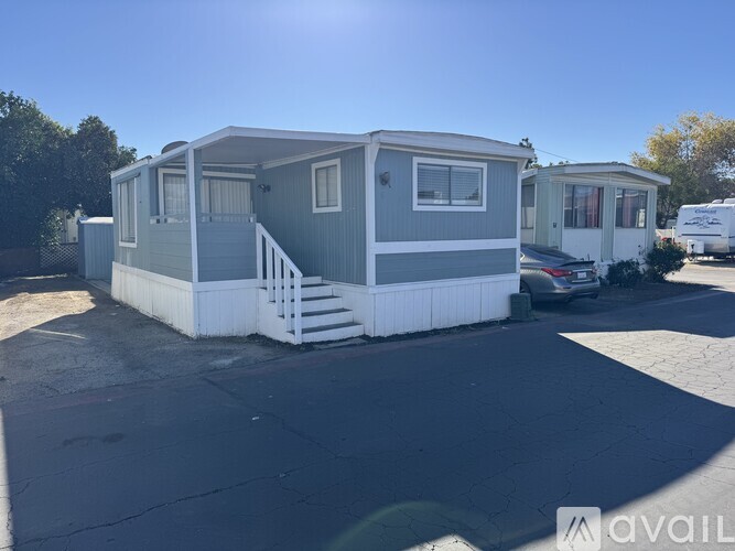 A grey and white mobile home with a car parked in front.