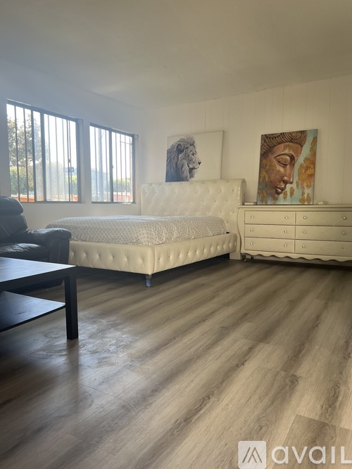 A bedroom with a white bed, a black chair, and a painting on the wall.