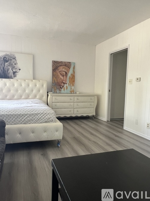 A bedroom with a white bed and a white dresser with a painting on it.