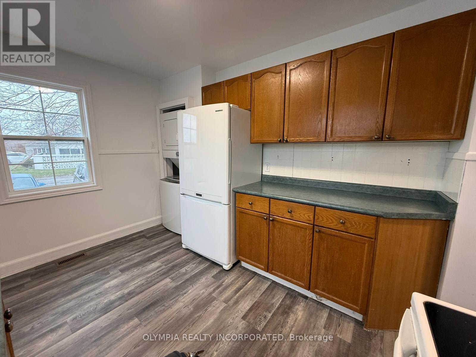 A kitchen with a white fridge, wooden cabinets, and a window.