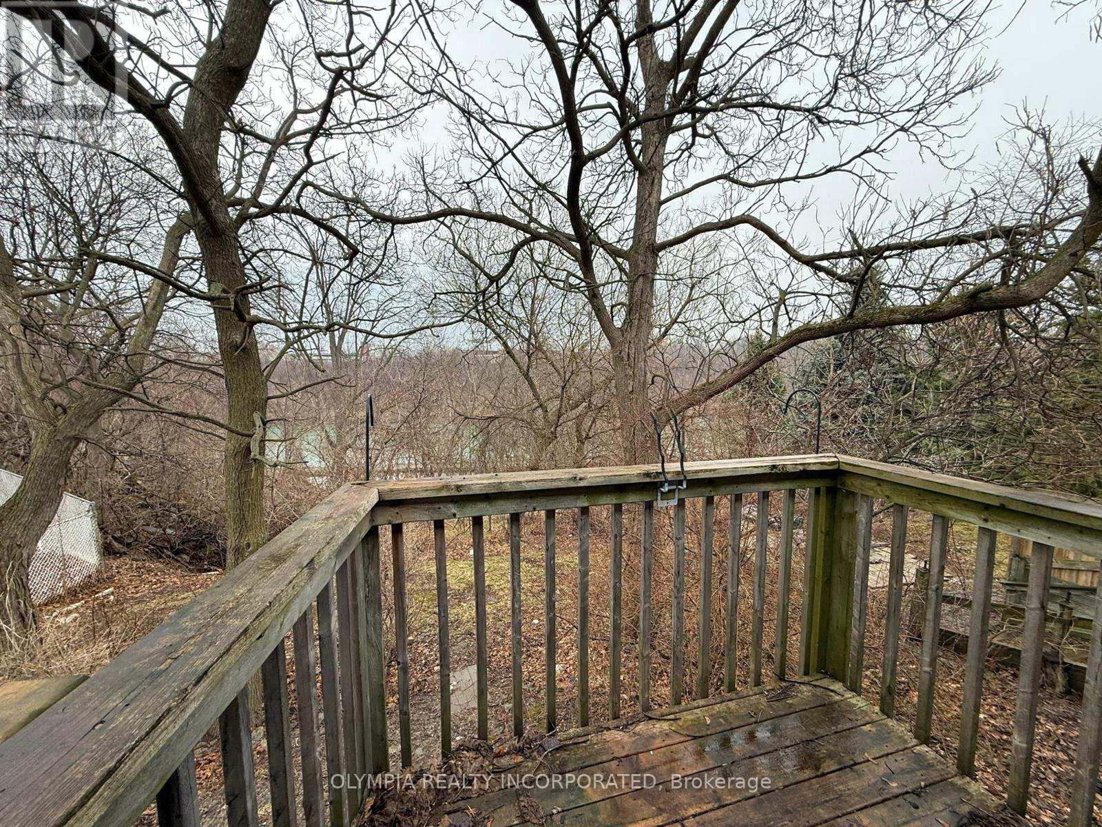 A wooden deck with a railing and bare trees in the background.