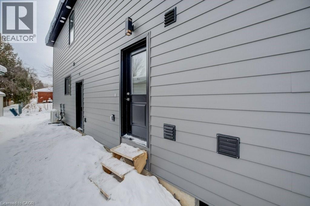 A house with a grey siding and a black door is shown with snow on the ground.