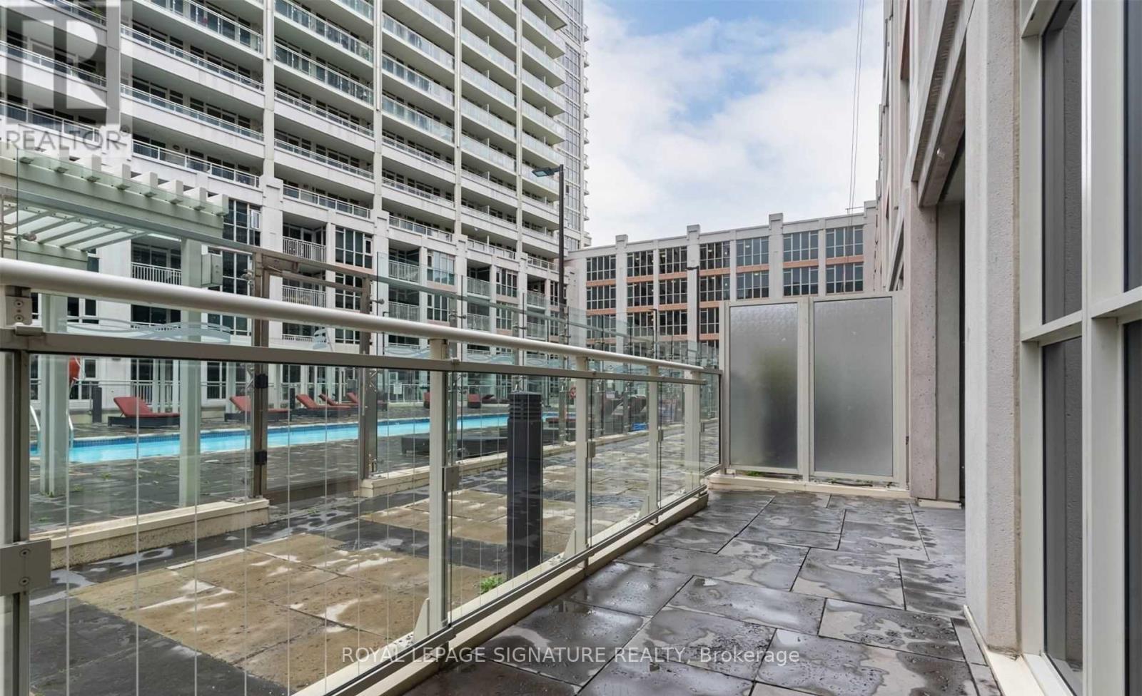 A balcony with a glass railing and a pool in the background.