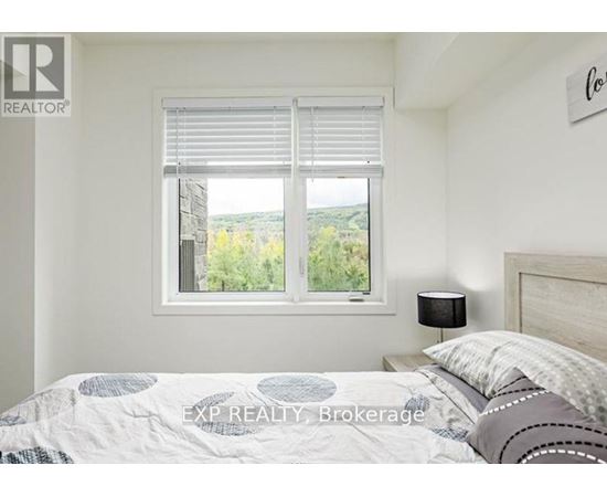 A bedroom with a bed, a window with blinds, and a lamp on the nightstand.