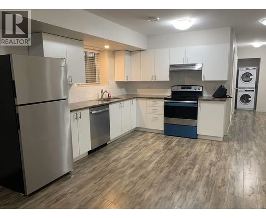 A modern kitchen with a stainless steel refrigerator and wooden flooring.