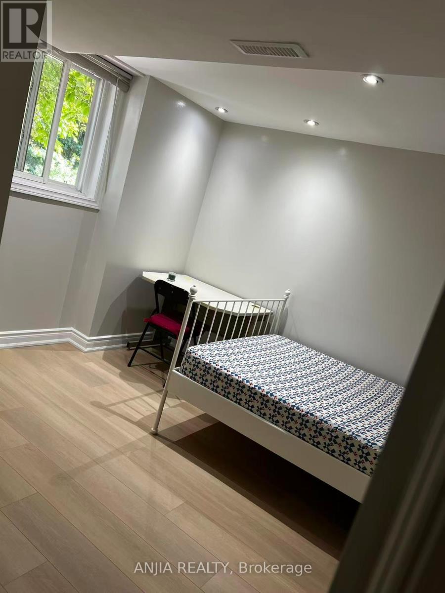 A baby crib sits in a corner of a room with light wood flooring and white walls.