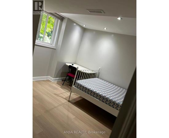 A baby crib sits in a corner of a room with light wood flooring and white walls.