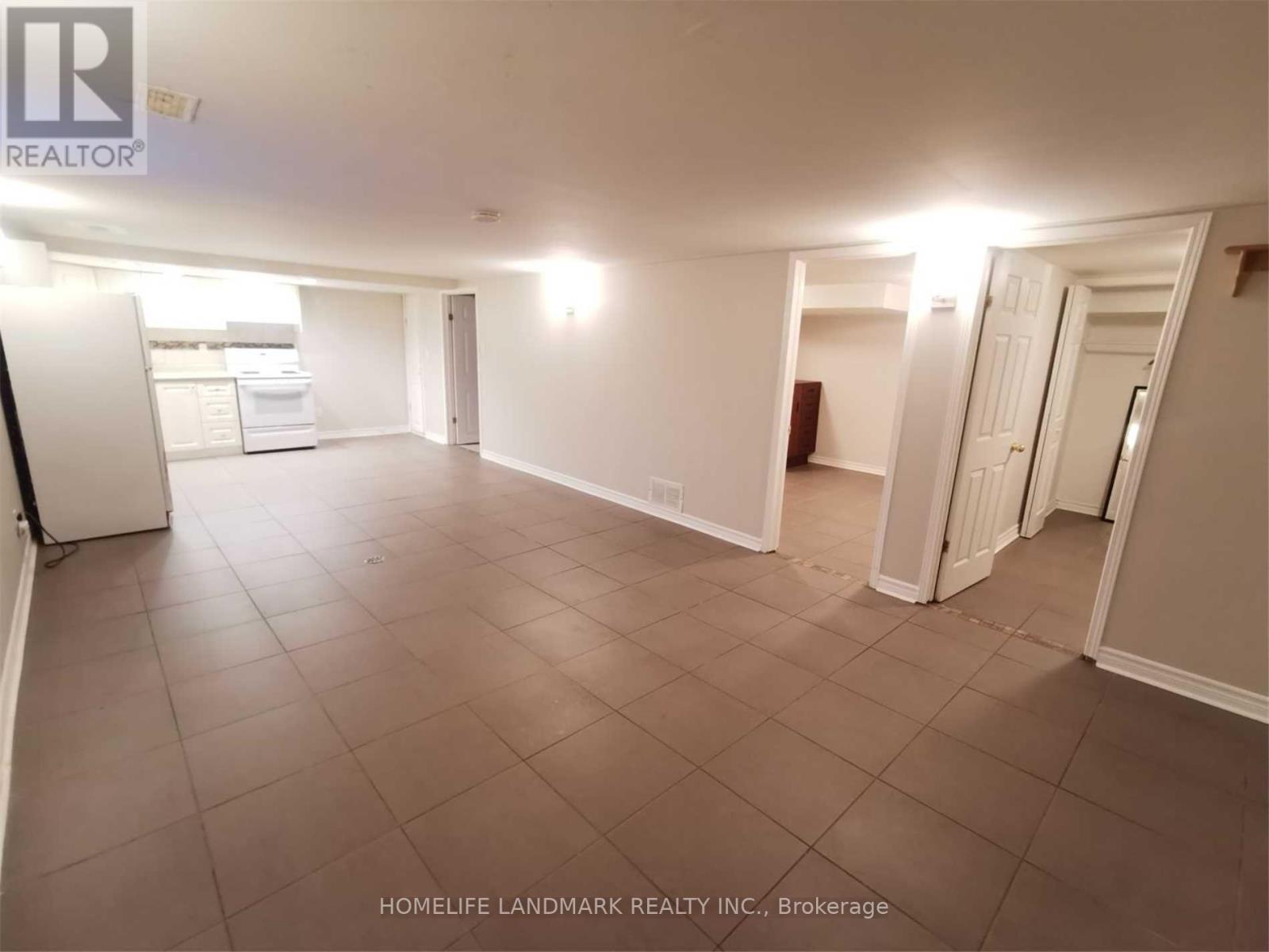 A spacious room with tile flooring and white walls, with a refrigerator on the left side.