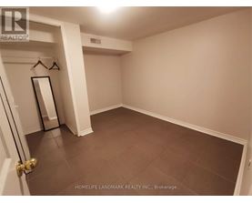 A room with a brown floor and white walls, with a door on the left and a coat rack with a mirror on the wall.