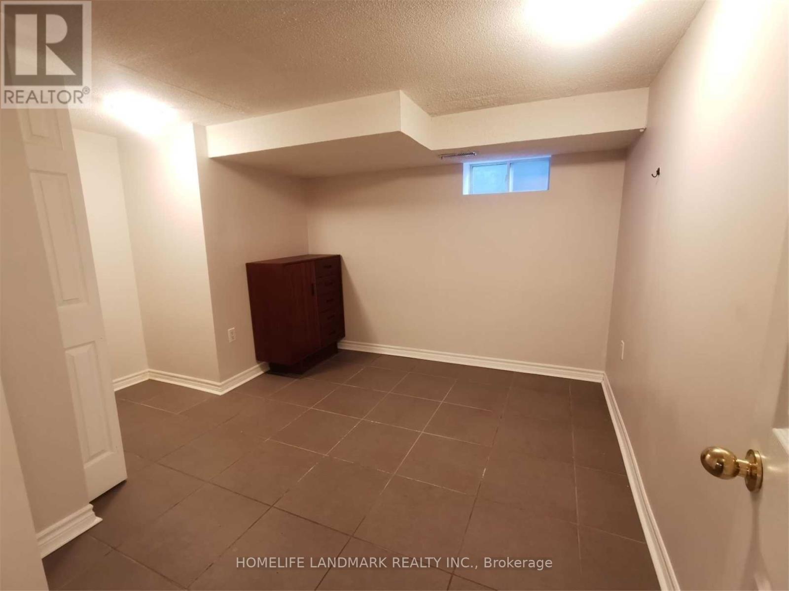 A room with a brown trash can and a small window.