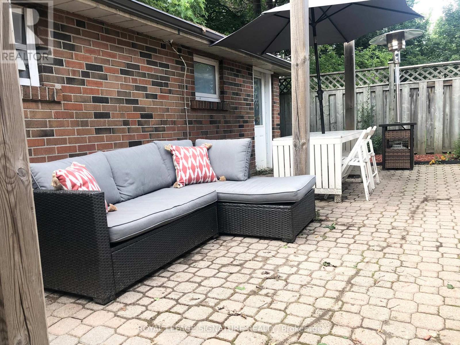 A black wicker couch with red and white pillows sits on a patio.