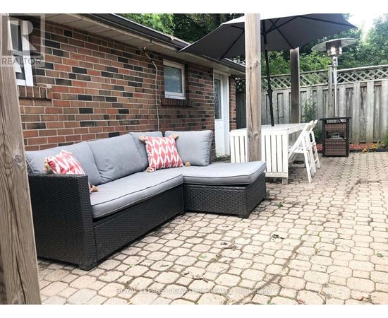 A black wicker couch with red and white pillows sits on a patio.