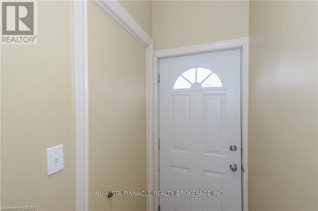 A white door with a window in the middle is in a room with a light switch on the wall.