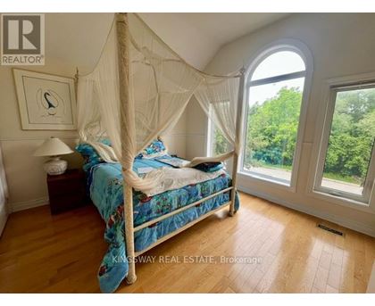 A bedroom with a canopy bed and a view of trees outside the window.