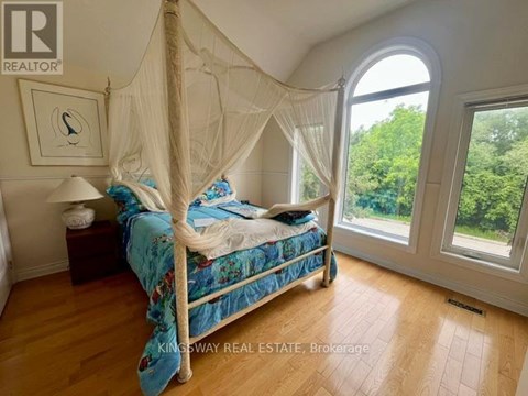 A bedroom with a canopy bed and a view of trees outside the window.