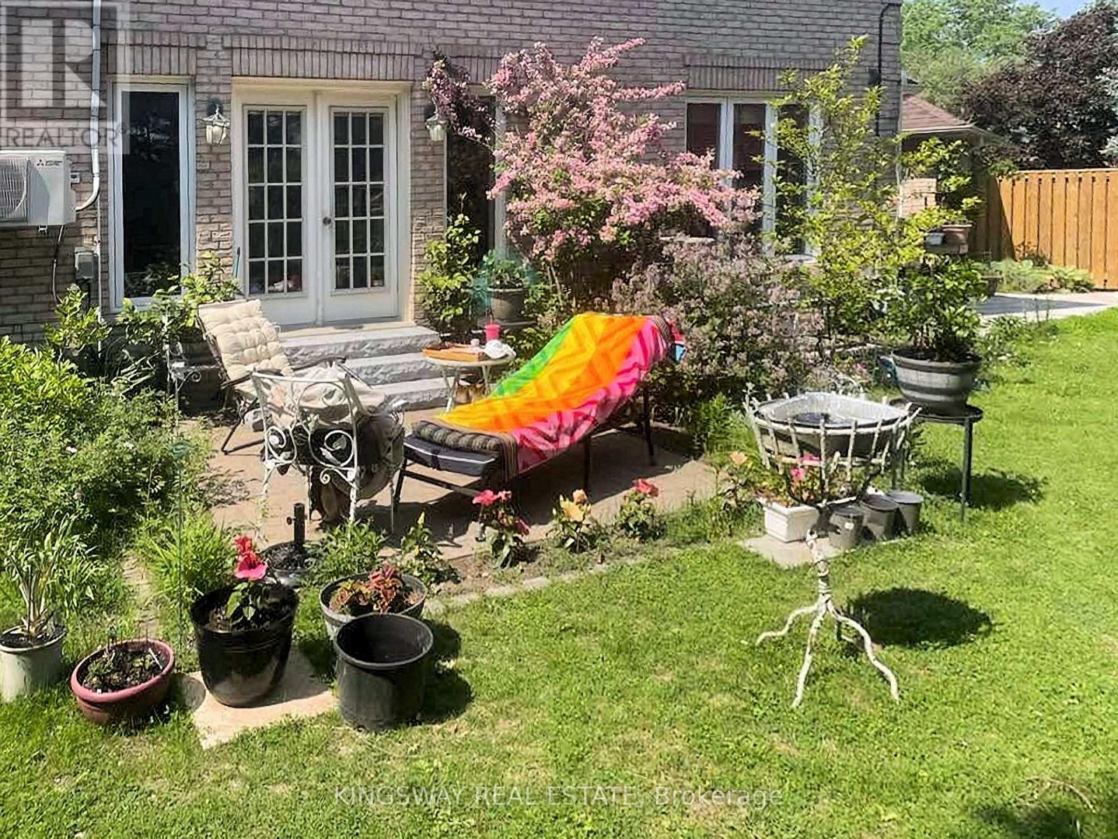 A backyard with a patio, lawn, and a few potted plants.