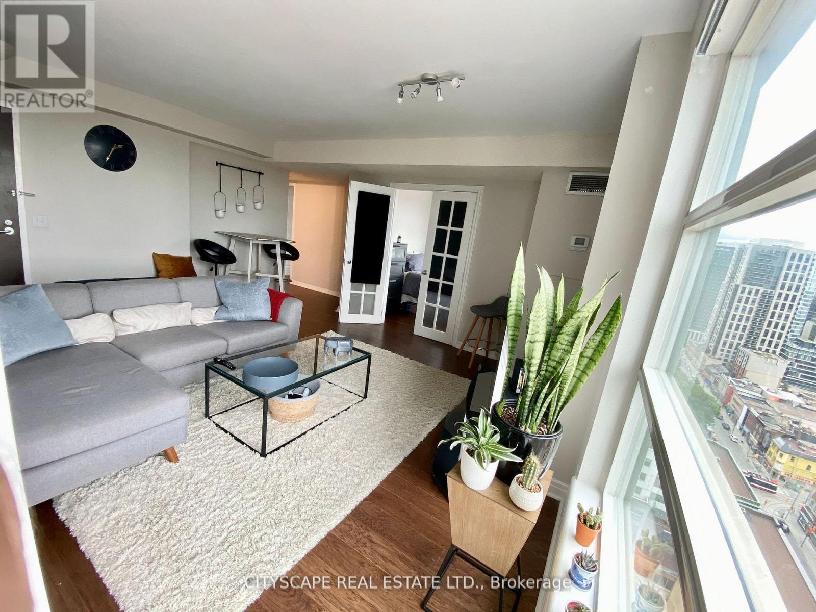A living room with a grey couch and a glass table with a plant on it.