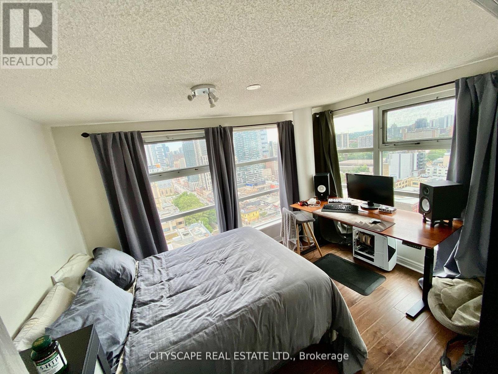 A bedroom with a bed, desk, and chair with a city view from the window.