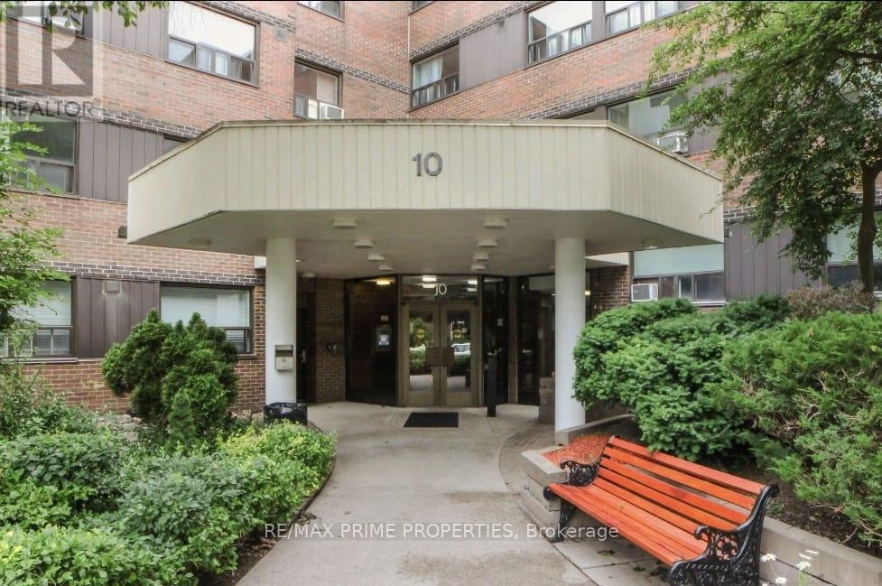The image shows the front of a building with the number 10 on it, surrounded by greenery and a bench.