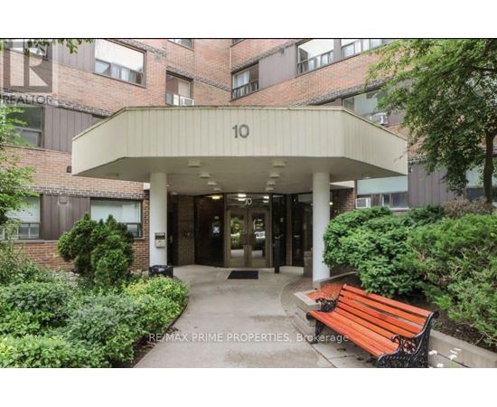 The image shows the front of a building with the number 10 on it, surrounded by greenery and a bench.