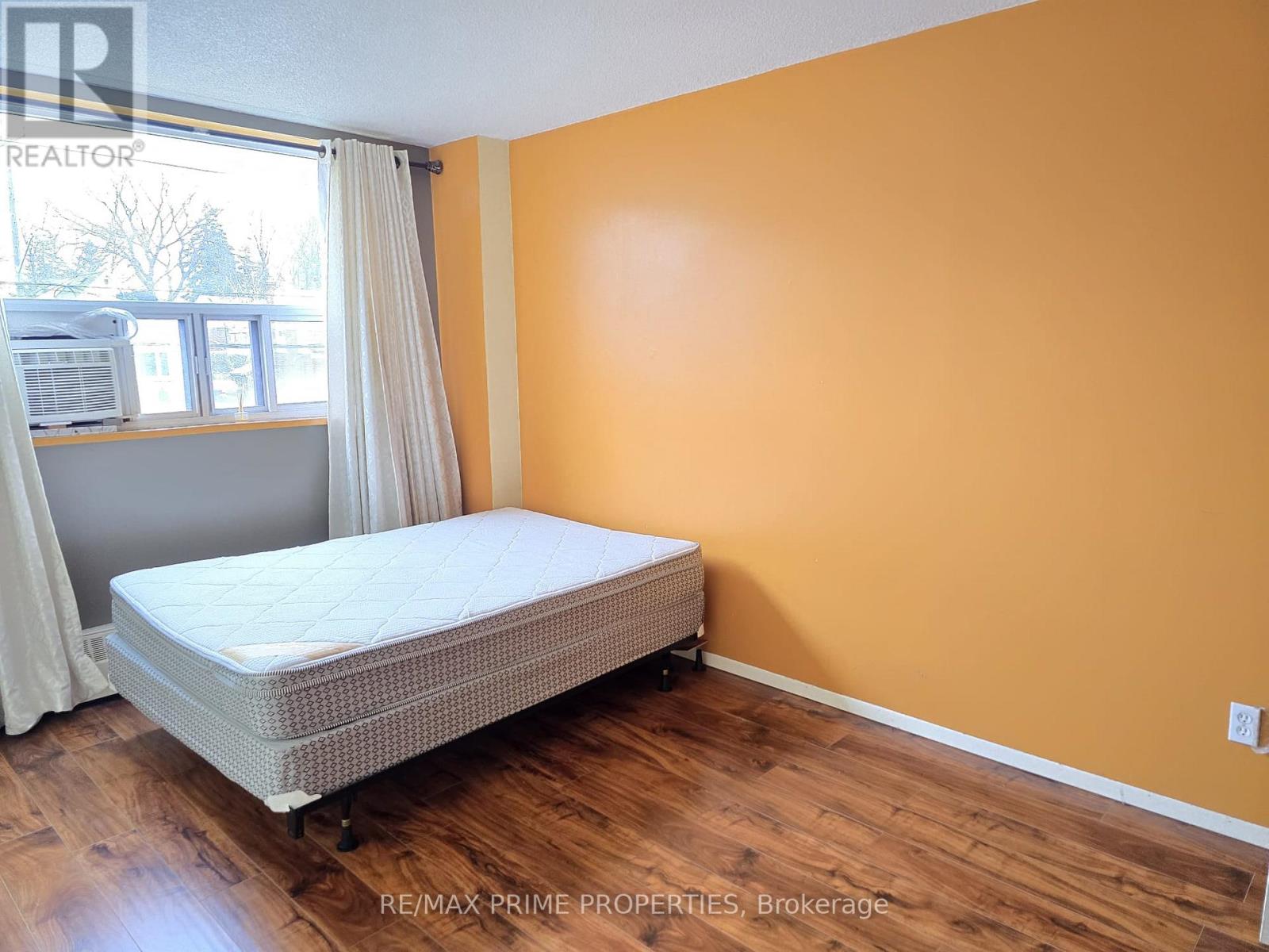 A bedroom with a bed, wooden floors, and a window with white curtains.