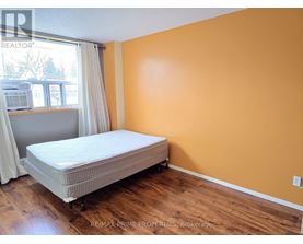 A bedroom with a bed, wooden floors, and a window with white curtains.