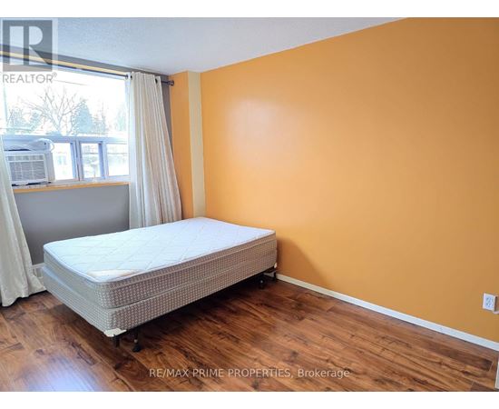 A bedroom with a bed, wooden floors, and a window with white curtains.