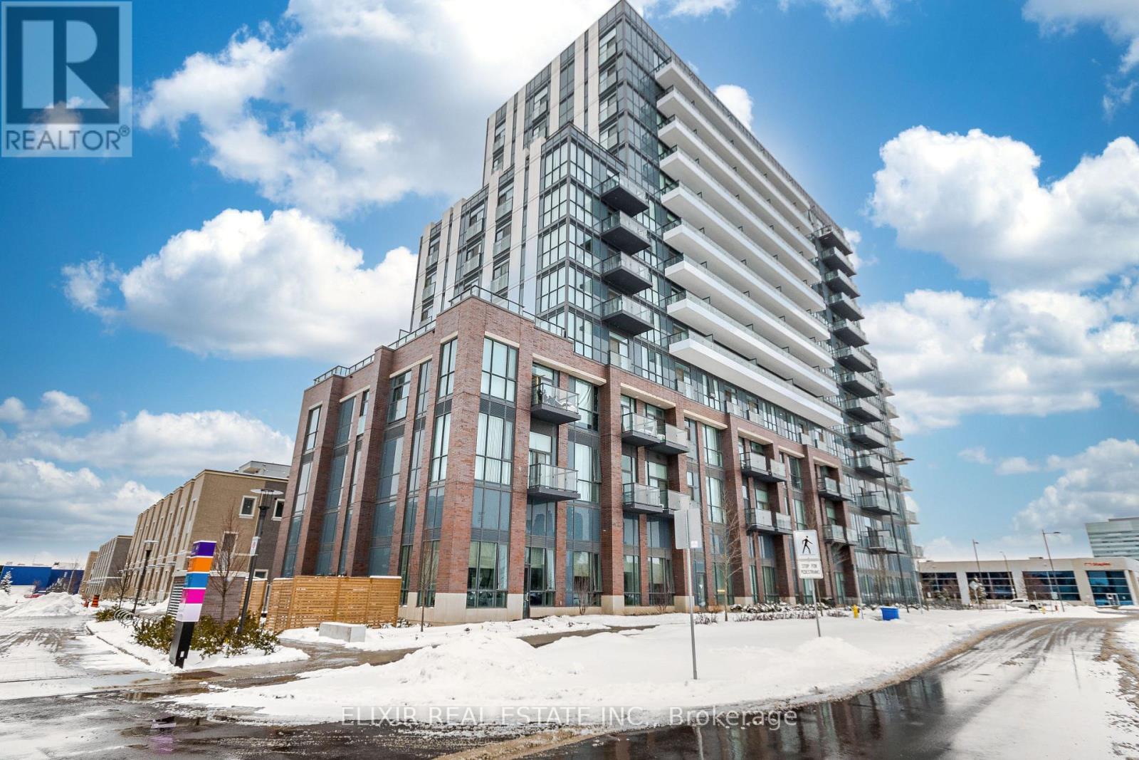 A modern multi-story building with a glass facade stands under a blue sky with clouds.