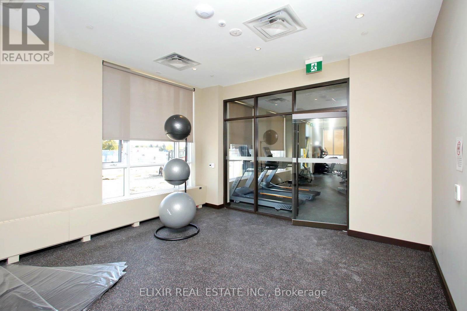 A room with a grey carpet and a glass door leading to a gym.