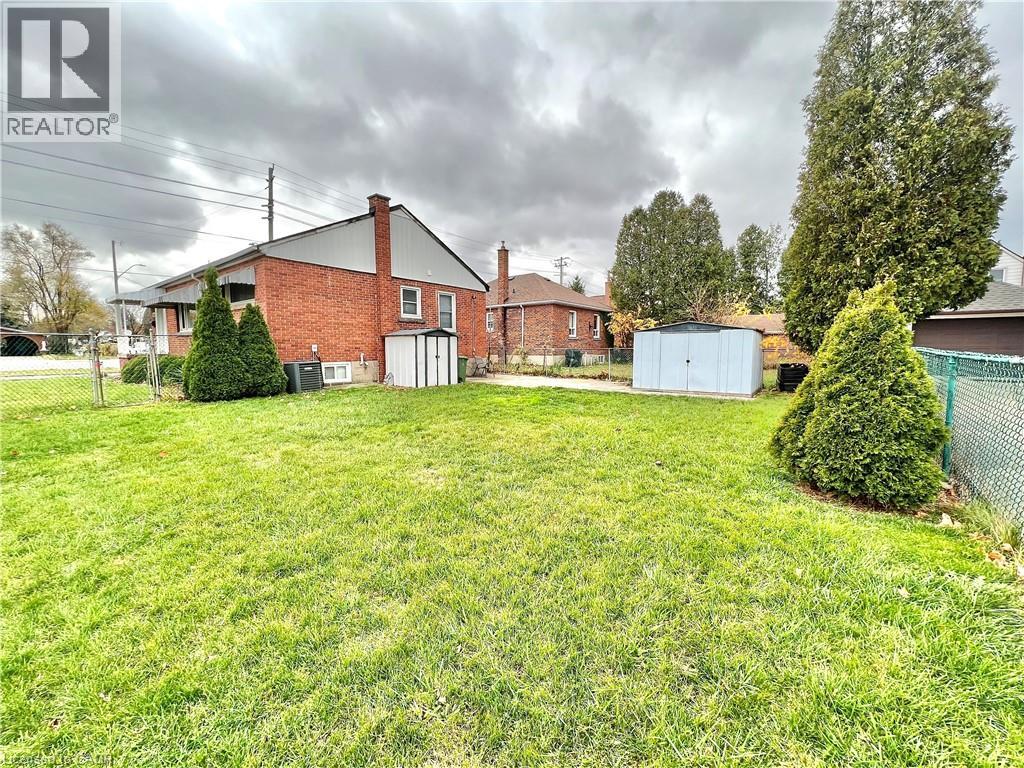 A large grassy yard with a house and a shed in the background.