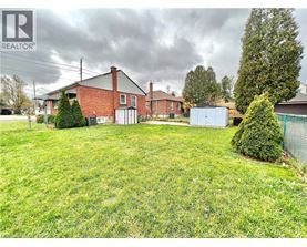 A large grassy yard with a house and a shed in the background.