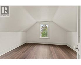 A room with wooden flooring and a window showing trees outside.