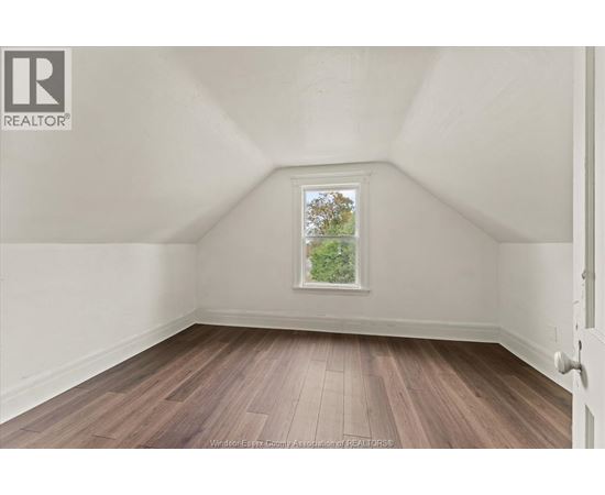A room with wooden flooring and a window showing trees outside.