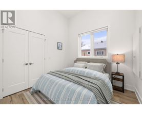 A bedroom with a bed, a nightstand with a lamp, and a window showing a view of a house.