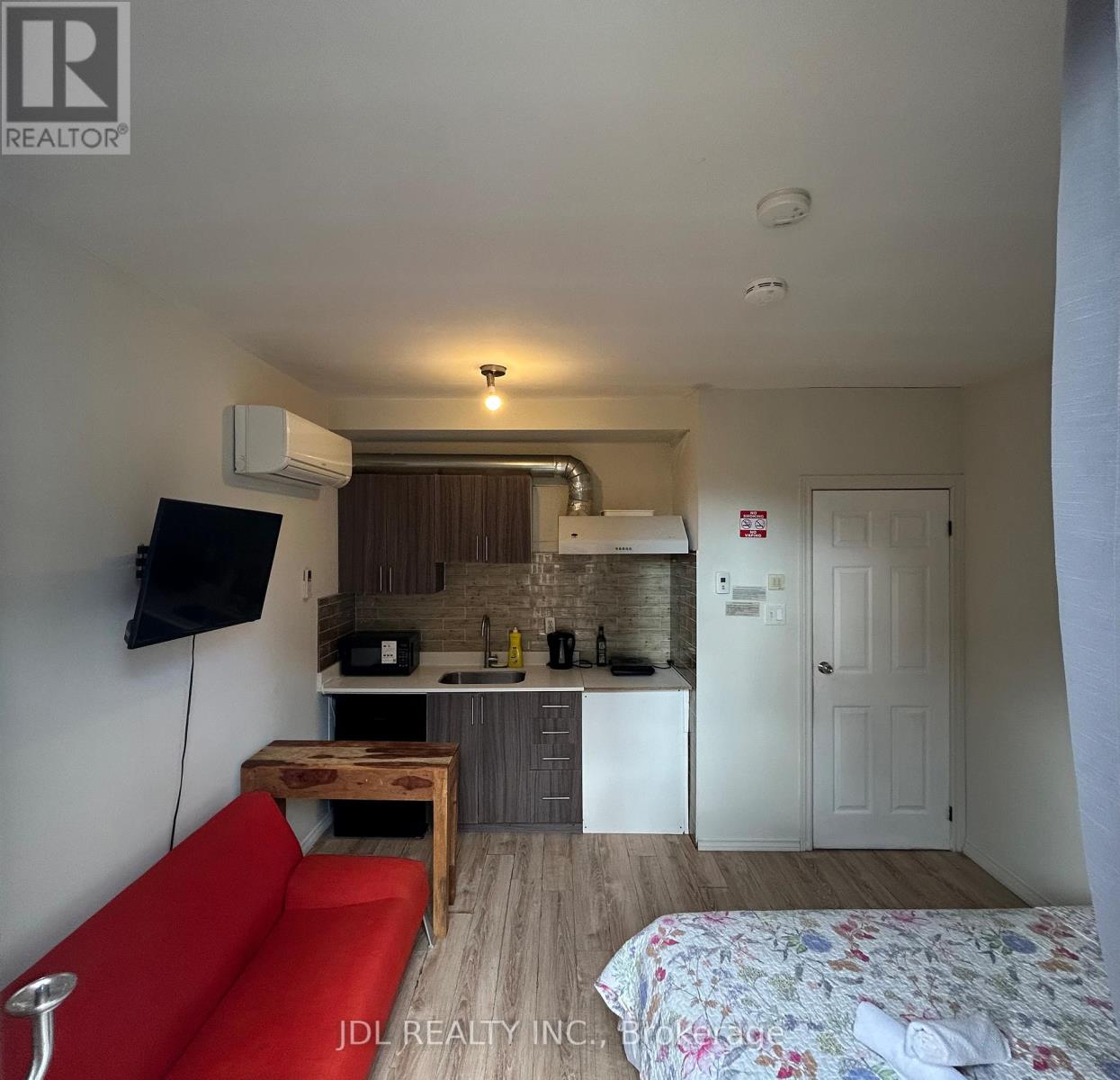 A small room with a red couch, a bed, a table, and a television.