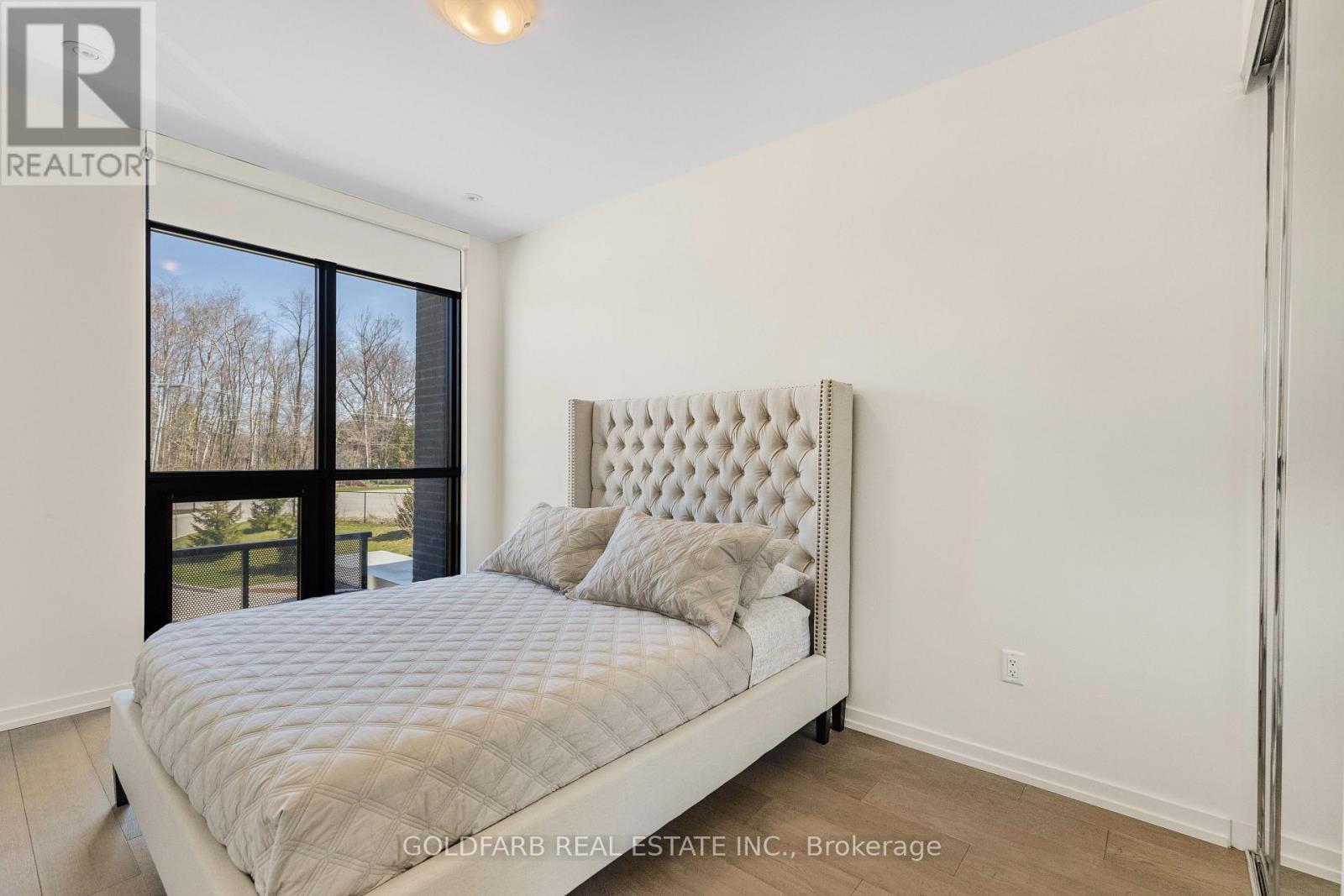 A bedroom with a large bed and a window overlooking a tree-lined area.
