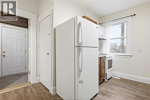 A white refrigerator stands in a kitchen with a wooden floor and white walls.