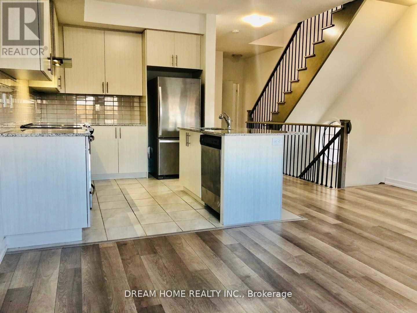 A kitchen with wooden floors and a staircase in the background.