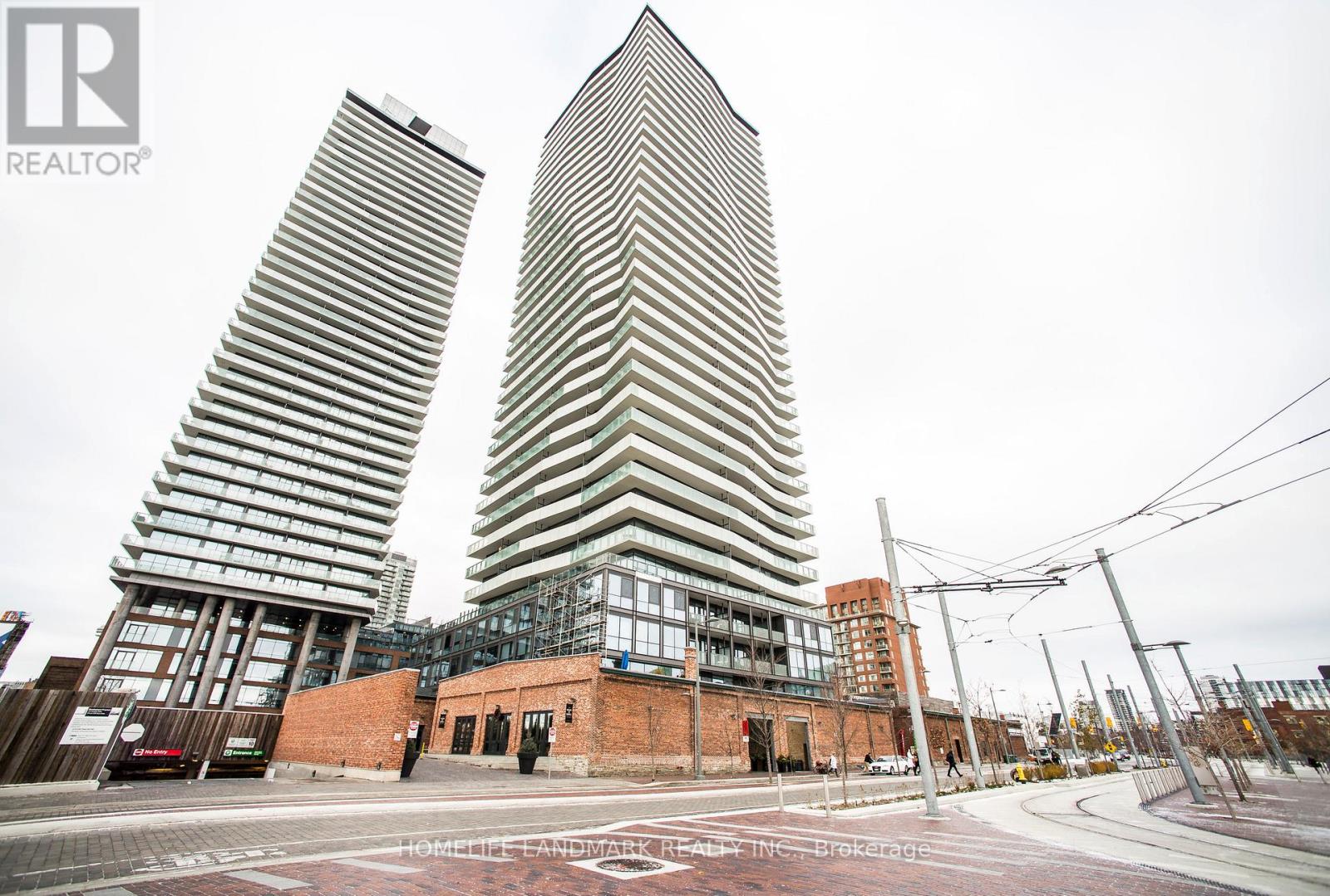 Two modern buildings stand side by side with a red brick building in the foreground.