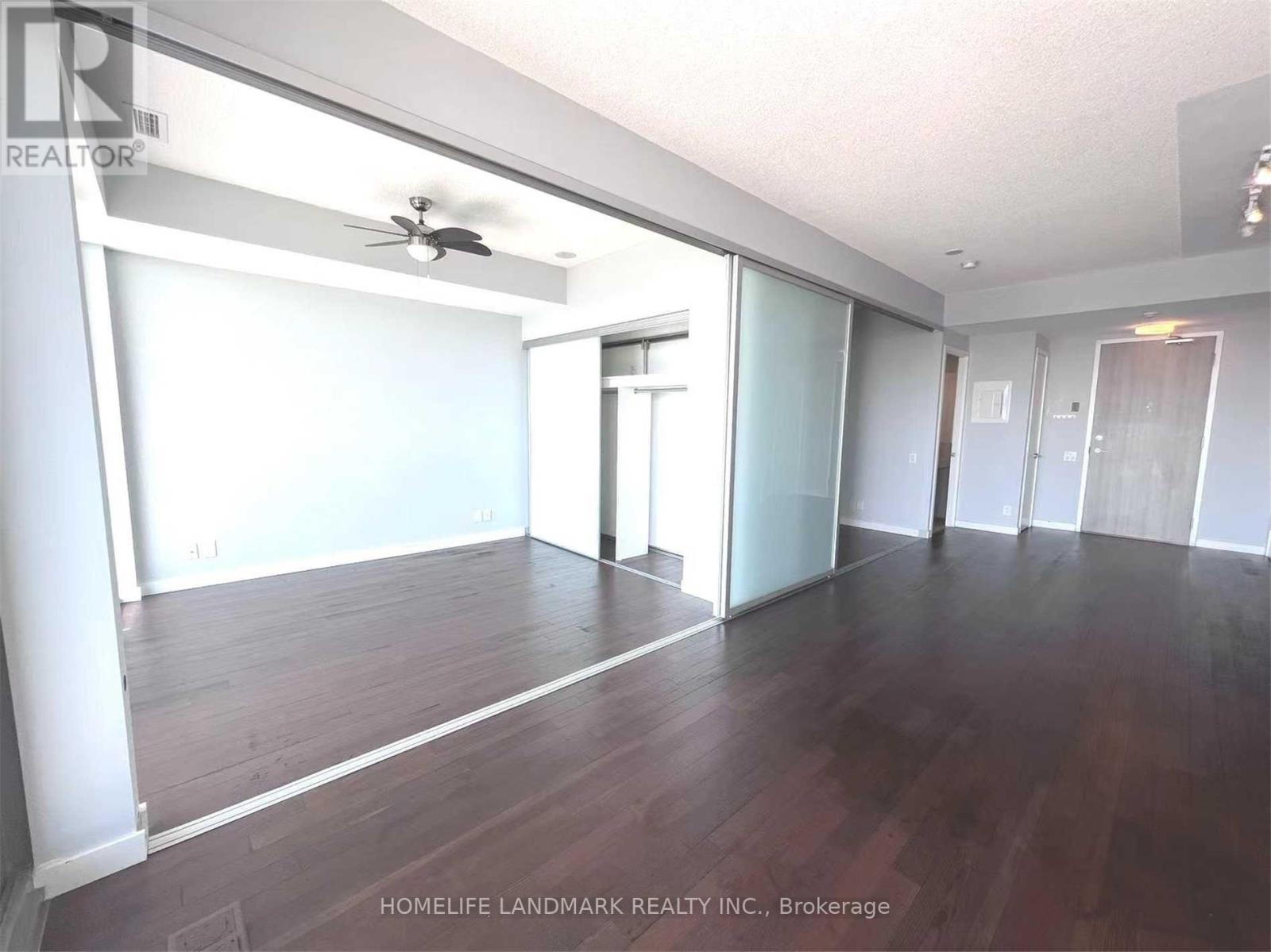 A spacious room with wooden floors and a ceiling fan.