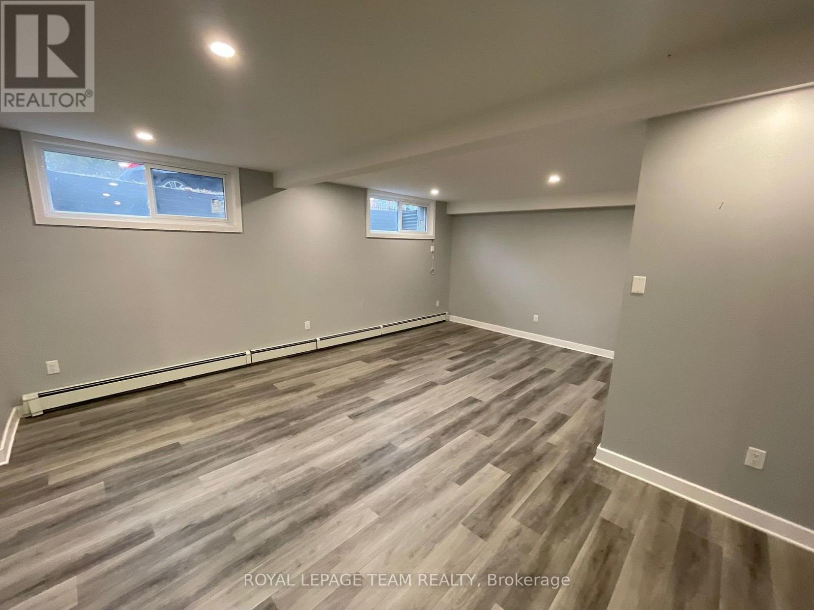 A room with grey wooden flooring and two windows.