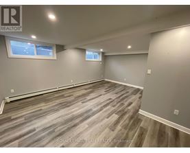 A room with grey wooden flooring and two windows.