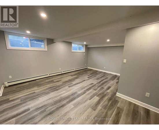 A room with grey wooden flooring and two windows.