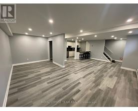 A spacious room with wooden flooring and a bar area in the corner.