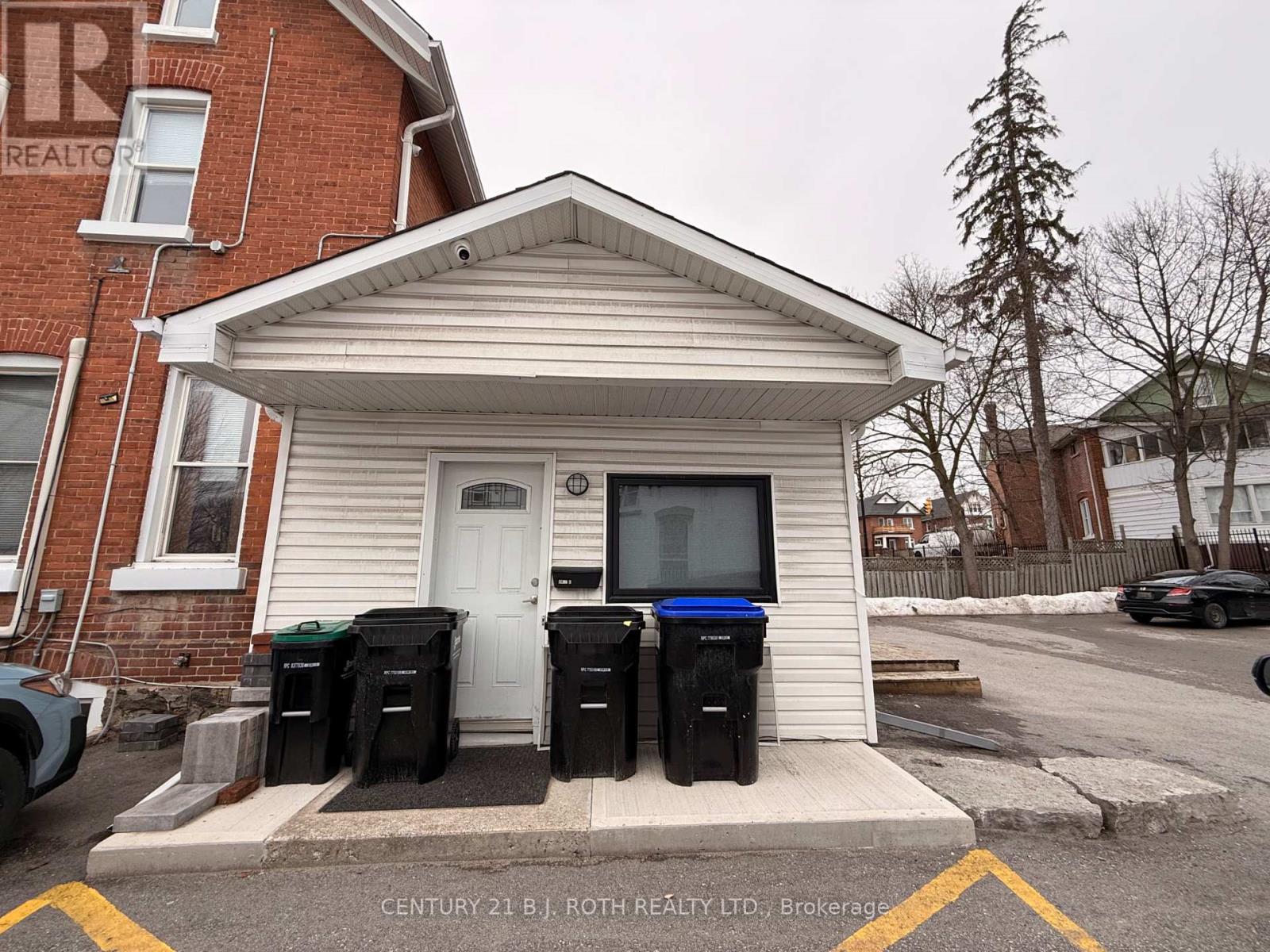 A small white building with a black trash can in front of it.
