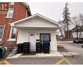 A small white building with a black trash can in front of it.