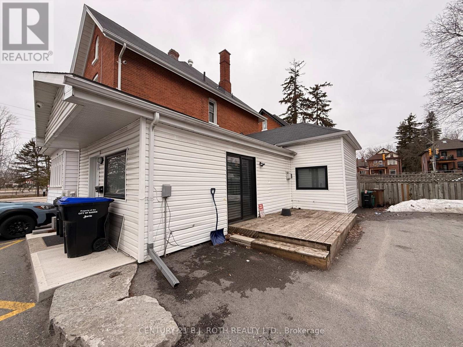 A white house with a black trash bin and a wooden deck.
