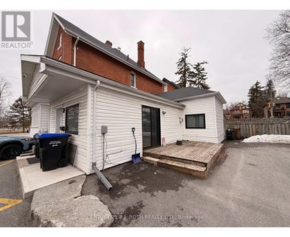 A white house with a black trash bin and a wooden deck.