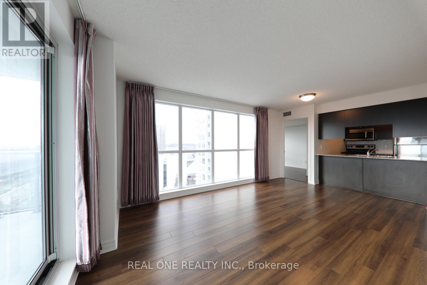 A spacious room with wooden flooring and large windows.